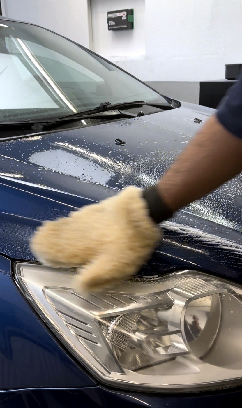 Handwäsche mit Waschhandschuh auf der Motorhaube eines blauen Fahrzeugs